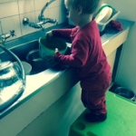 toddler stands on table and tries to wash dishes